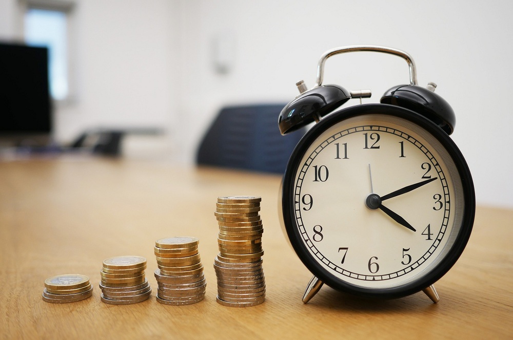 moedas empilhadas de forma crescente ao lado de um relógio em cima de uma mesa de escritório simbolizando a rentabilidade dos investimentos com a Selic em alta