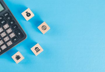Conceito financeiro com ícones em cubos de madeira, calculadora na tabela azul plana leigos